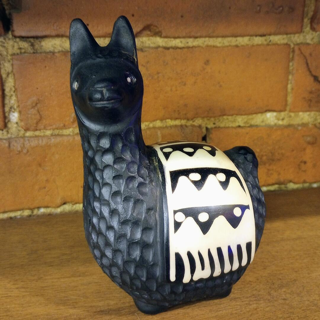 Black and white ceramic llama figurine against a brick wall.