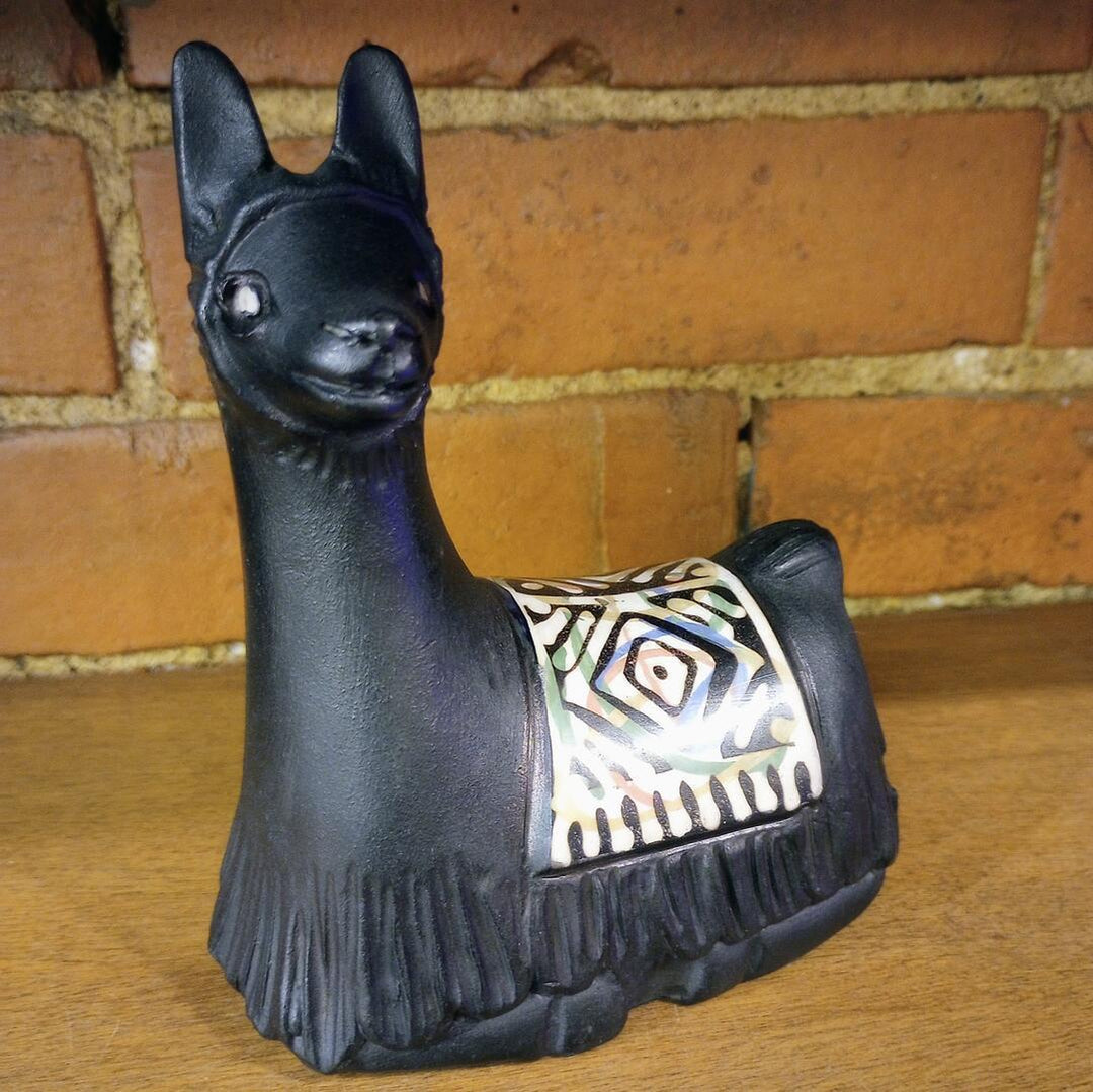 Black decorative llama figurine with a patterned saddle on a wooden surface with a brick wall background.