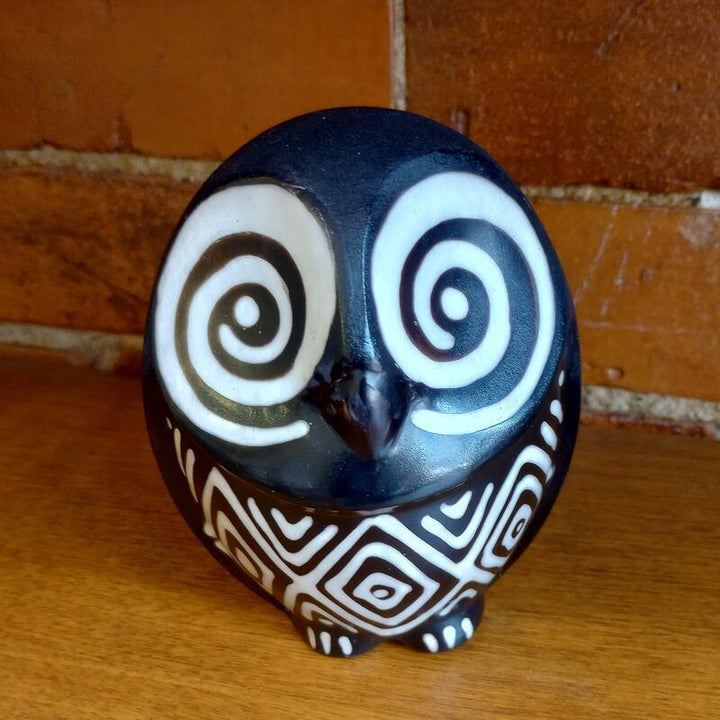 Decorative owl figurine with black, white, and brown patterns on a wooden surface.