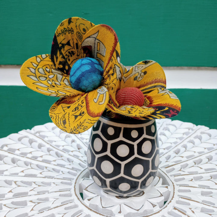 Decorative flower made of fabric with colorful centers in a black and white patterned vase on a textured surface.
