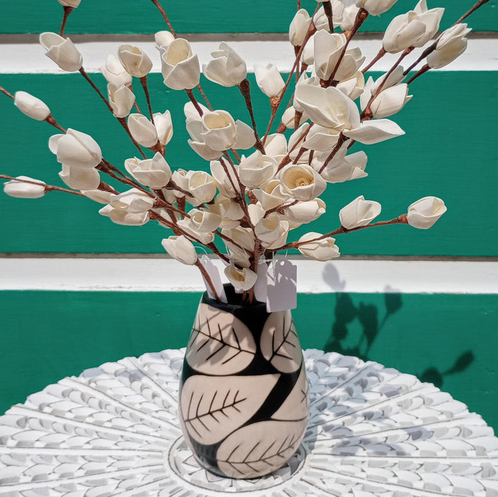 Decorative vase with white floral branches on a textured surface against a green background