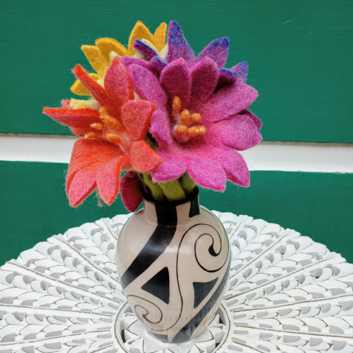 Colorful felt flowers in a decorative vase on a textured surface with a green background