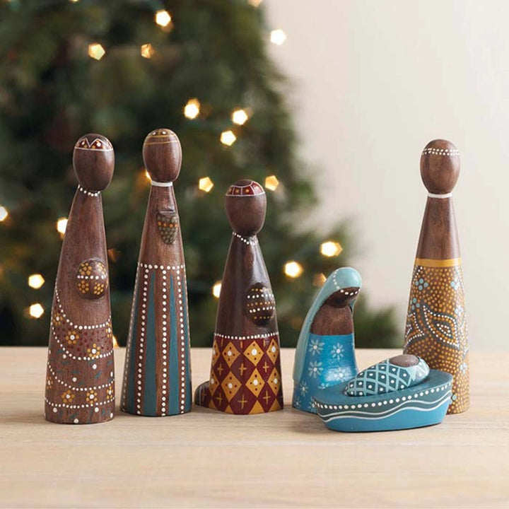 Wooden nativity scene figures with a decorated Christmas tree in the background