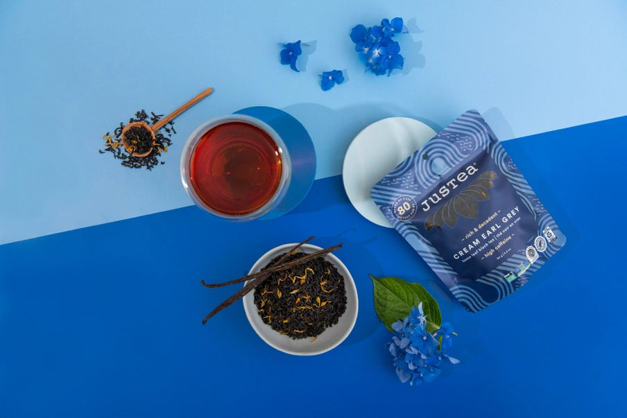 Tea cup, tea leaves, and JusTea earl grey tea package on a blue background