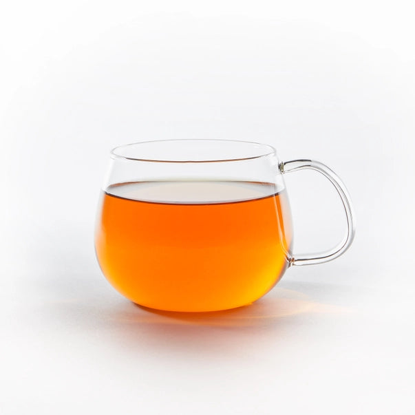 Clear glass mug filled with cream early grey tea on a white background