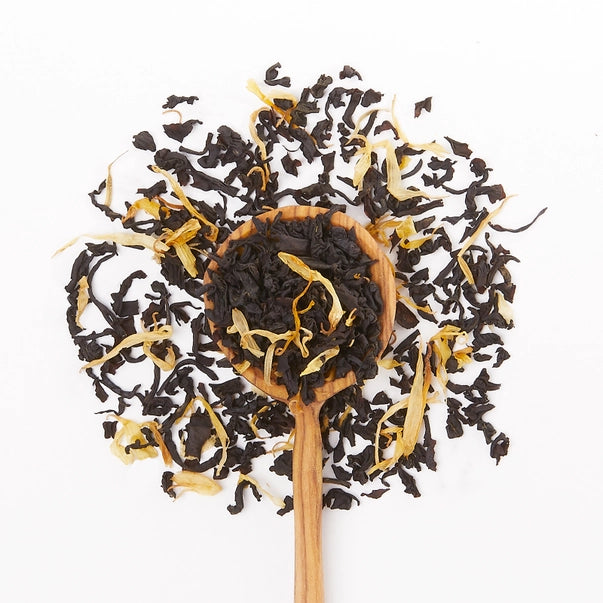Wooden spoon filled with cream earl grey tea leaves on a white background