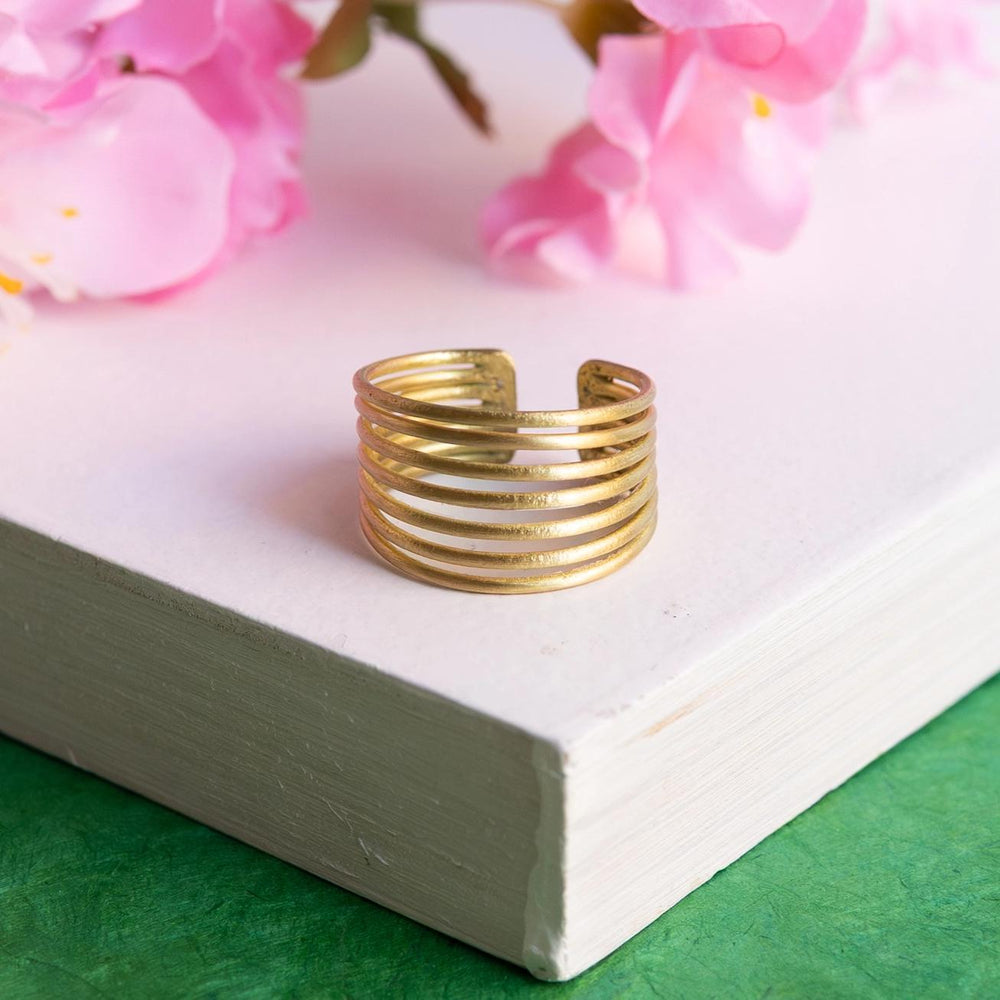 Gold crescendo ring on a white surface with pink flowers in the background