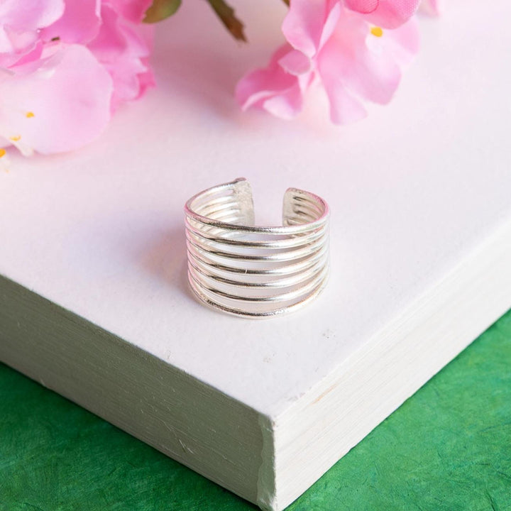Silver ring with multiple bands on a white surface with pink flowers in the background