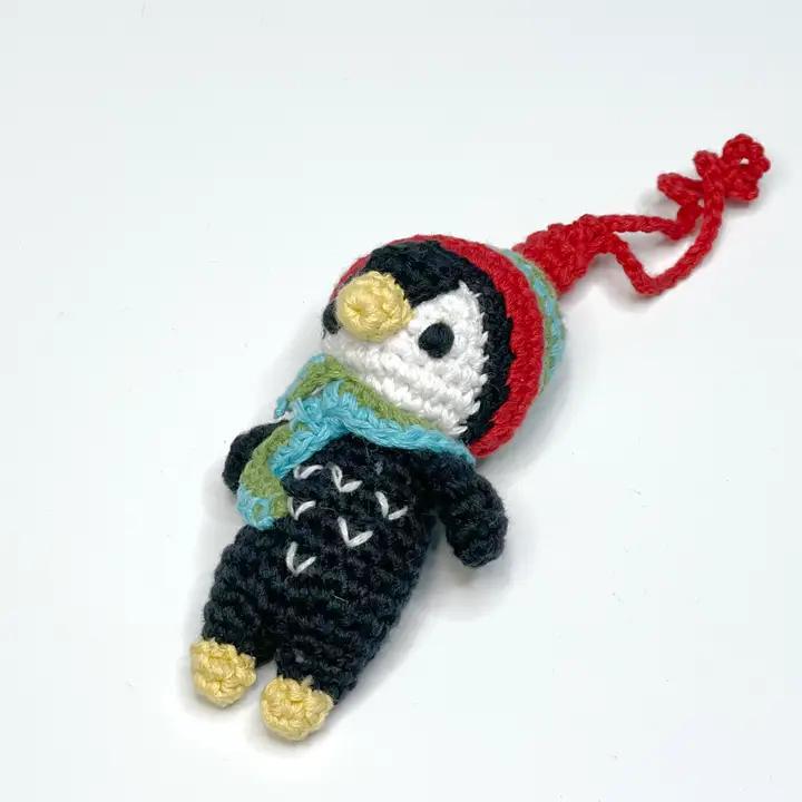 Crocheted penguin ornament with a red hat on a white background