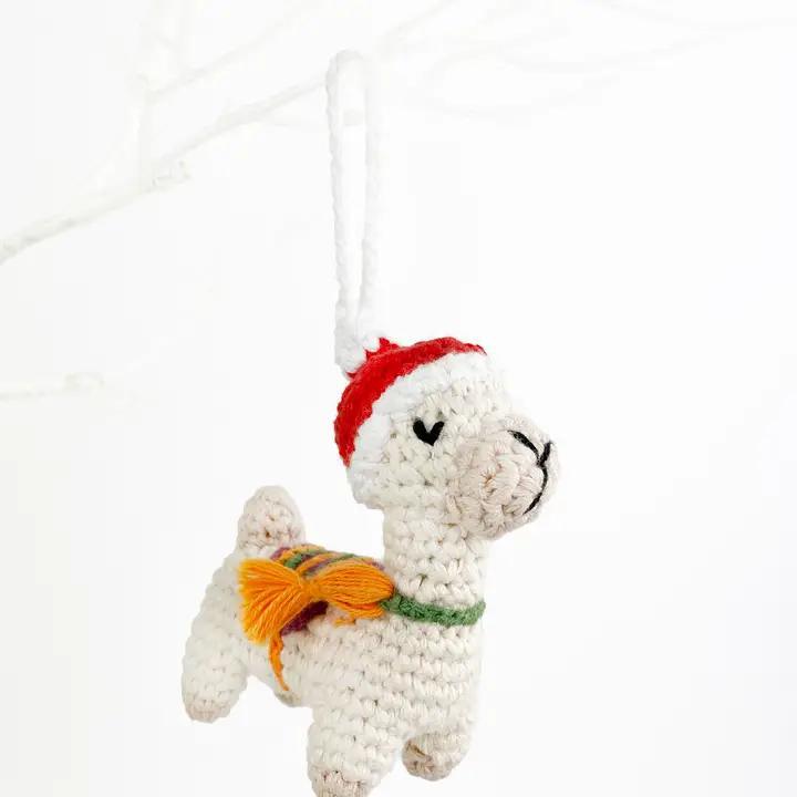 Crocheted llama ornament with a red hat and green scarf on a white background