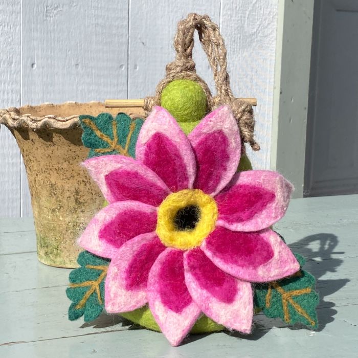 Felted pink flower with a yellow center on a green base, attached to a woven basket.