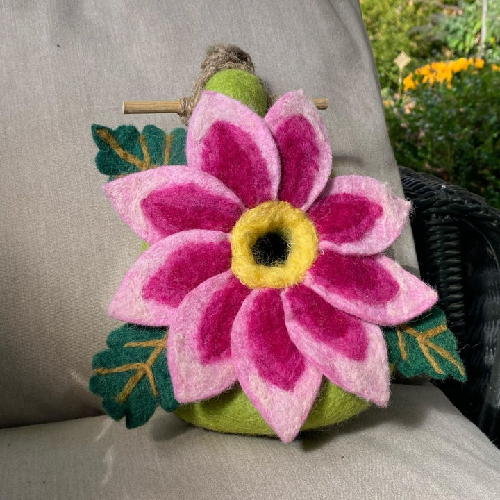 Felted flower pillow with pink petals and green leaves on a cushion outdoors.