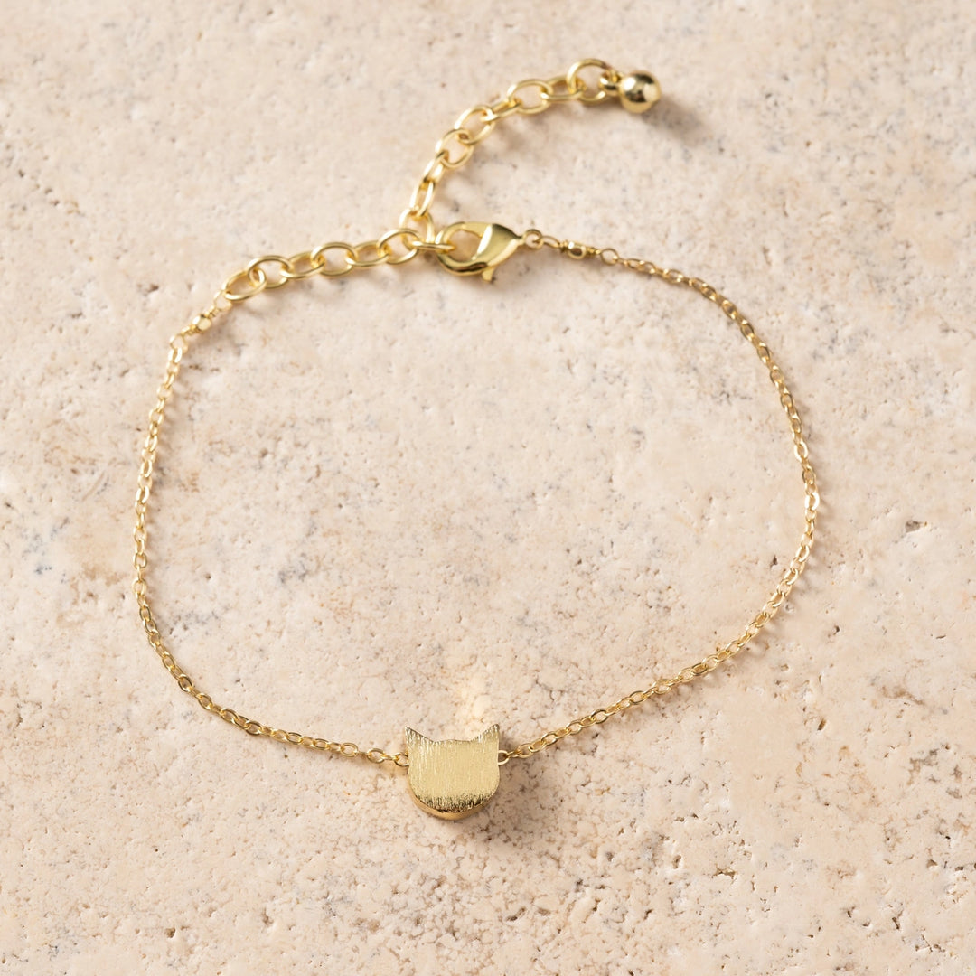 Gold bracelet with a cat-shaped charm on a beige background