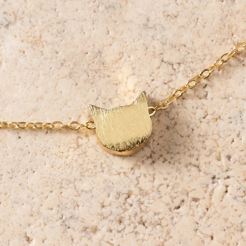 Gold cat-shaped pendant necklace on a beige textured background