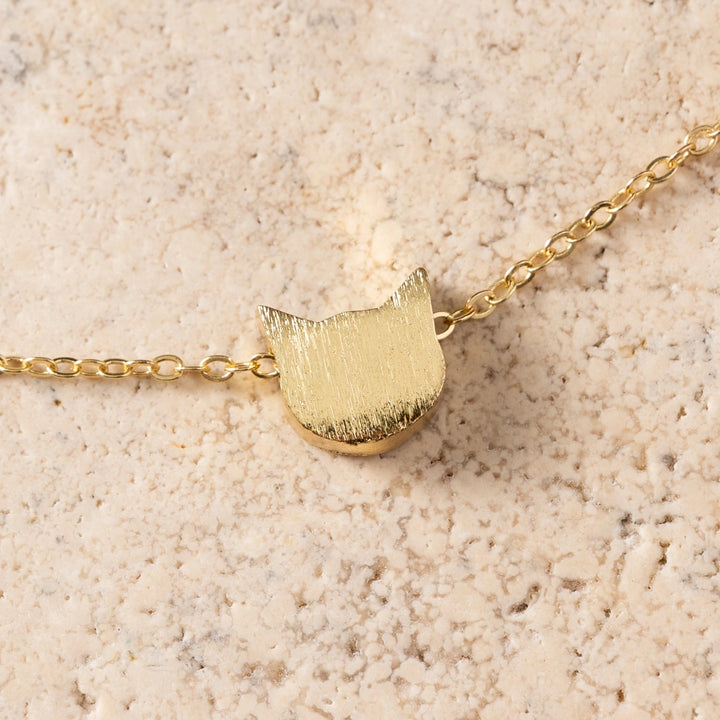Gold cat-shaped pendant necklace on a beige textured background