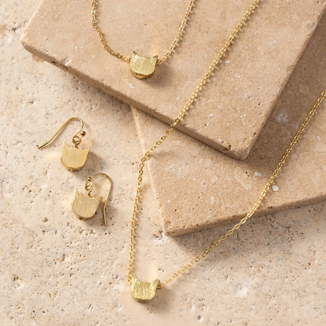 Gold jewelry set with necklace and earrings on a beige stone surface