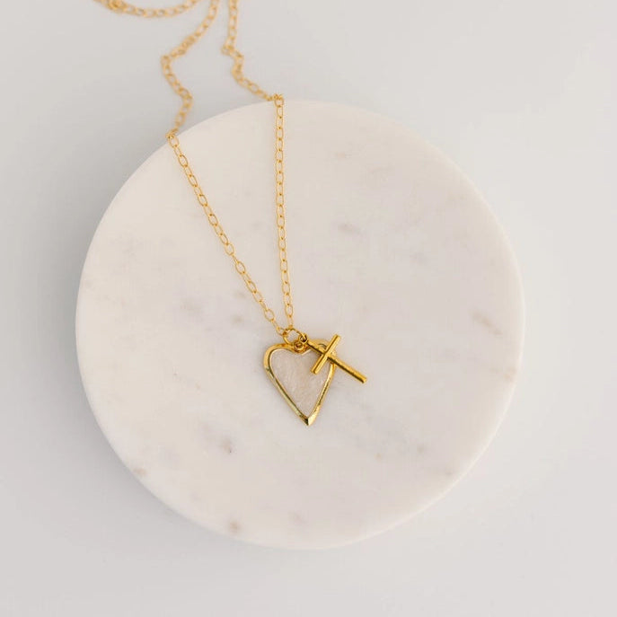 Gold necklace with a heart-shaped pendant and cross pendant on a marble base