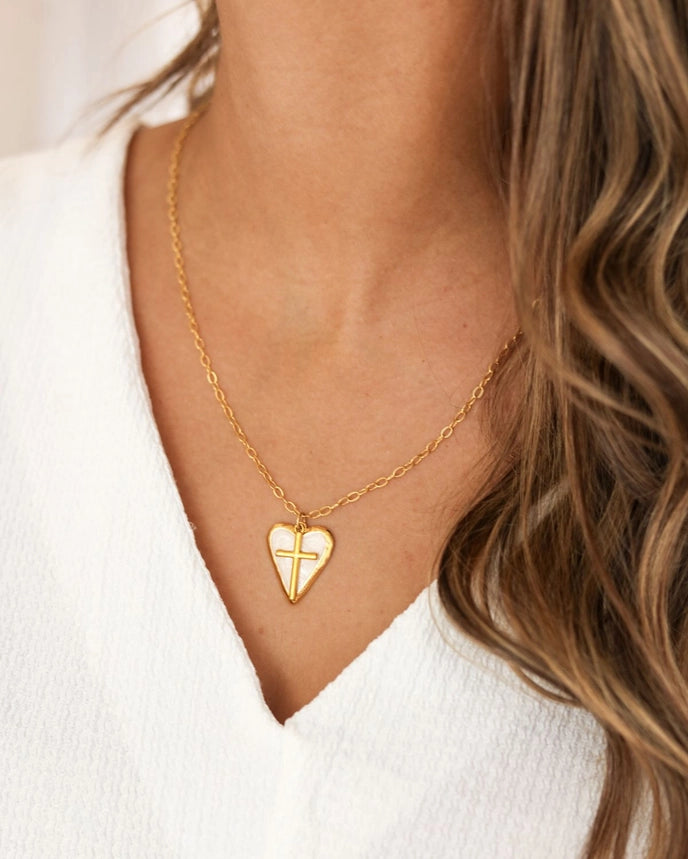 Gold necklace with a heart-shaped pendant and cross pendant worn by a person with wavy hair.