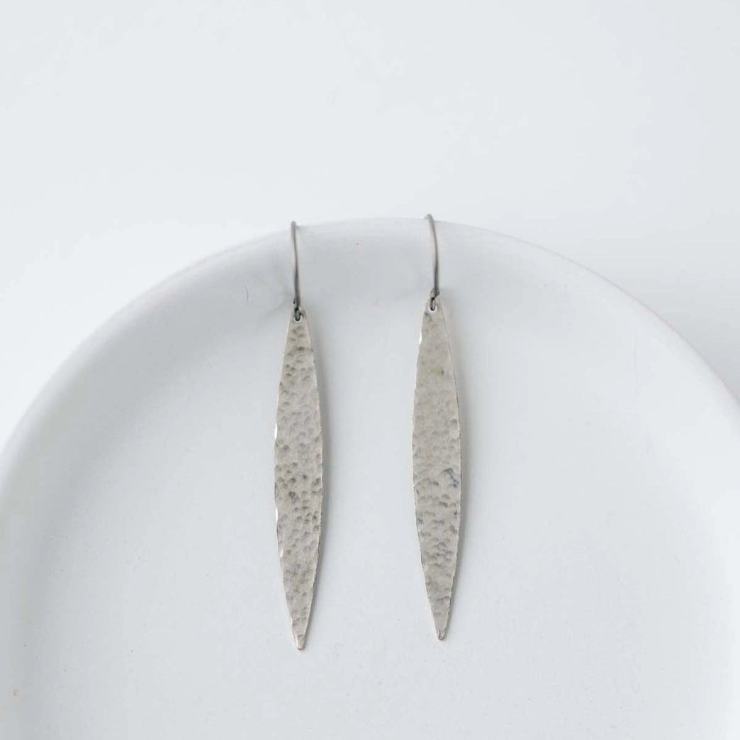 Pair of long, thin silver earrings on a white plate with a white background