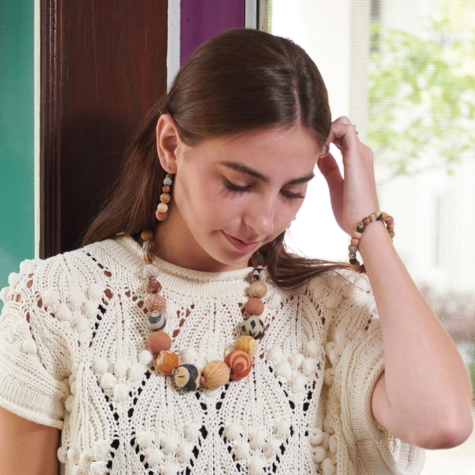 Woman wearing a desertscape bracelet, necklace, and earrings with a textured white top, indoors.