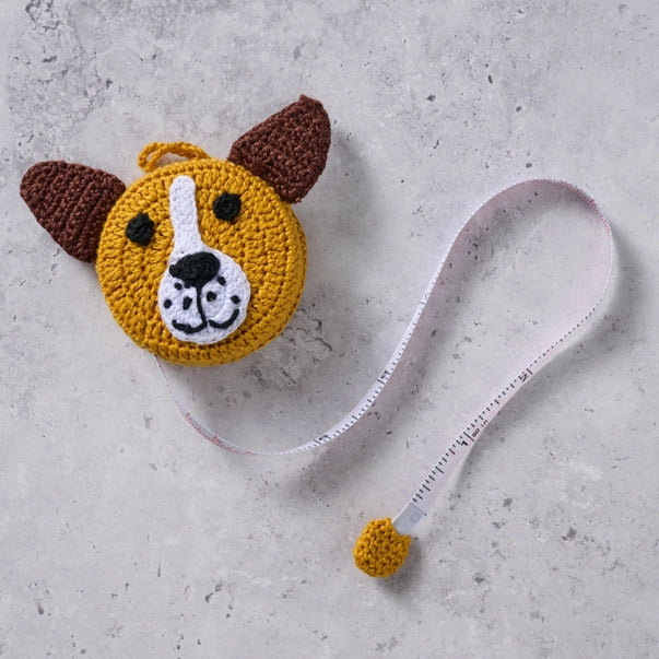 Crocheted dog face pouch with a measuring tape on a textured surface