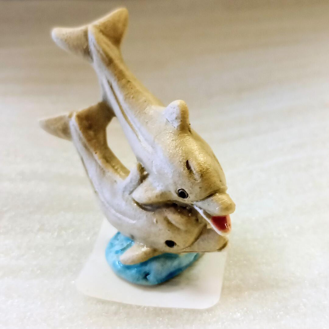 Two ceramic smiling dolphin figurines on a beige background