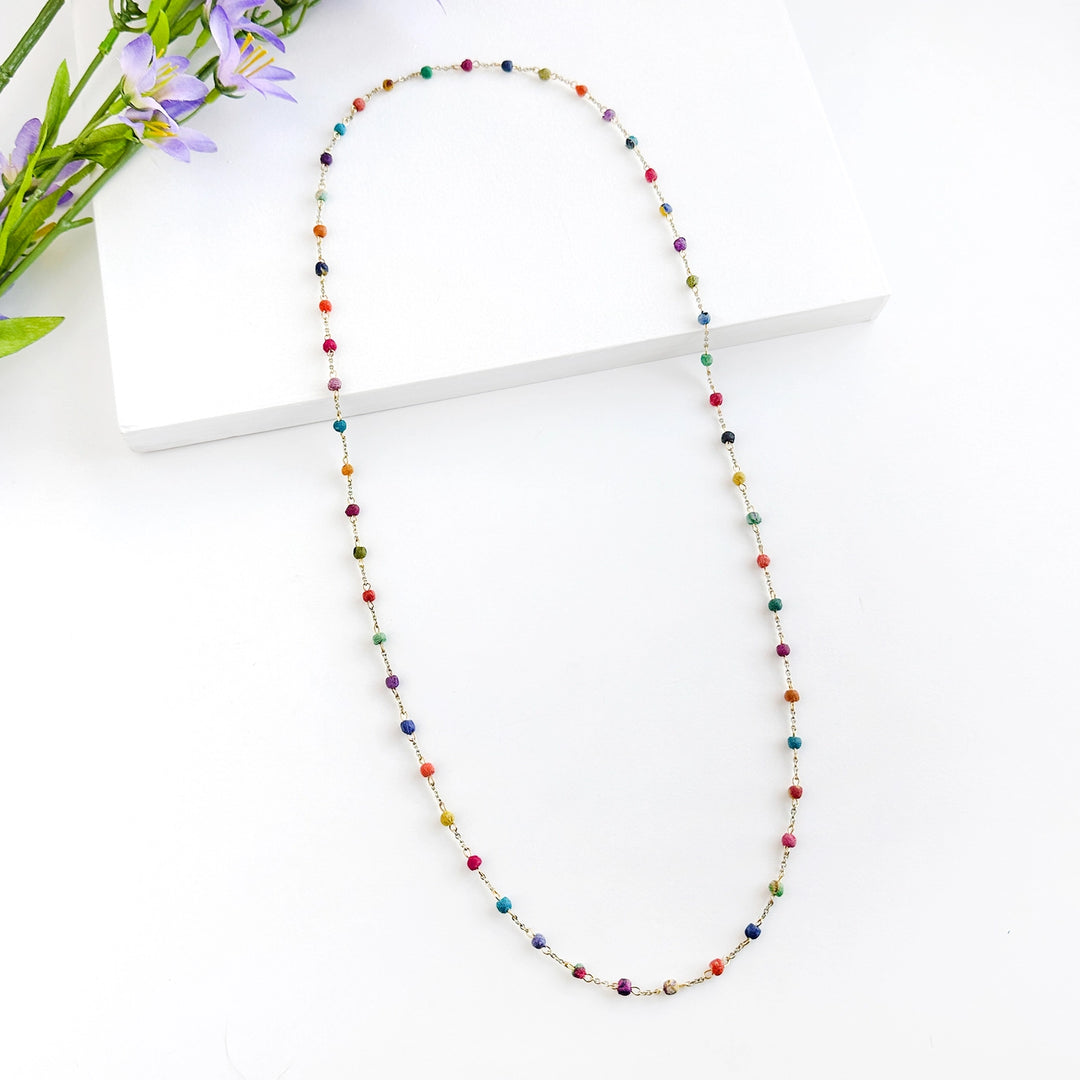 Colorful dotted Kantha milieu necklace on a white surface with flowers in the background