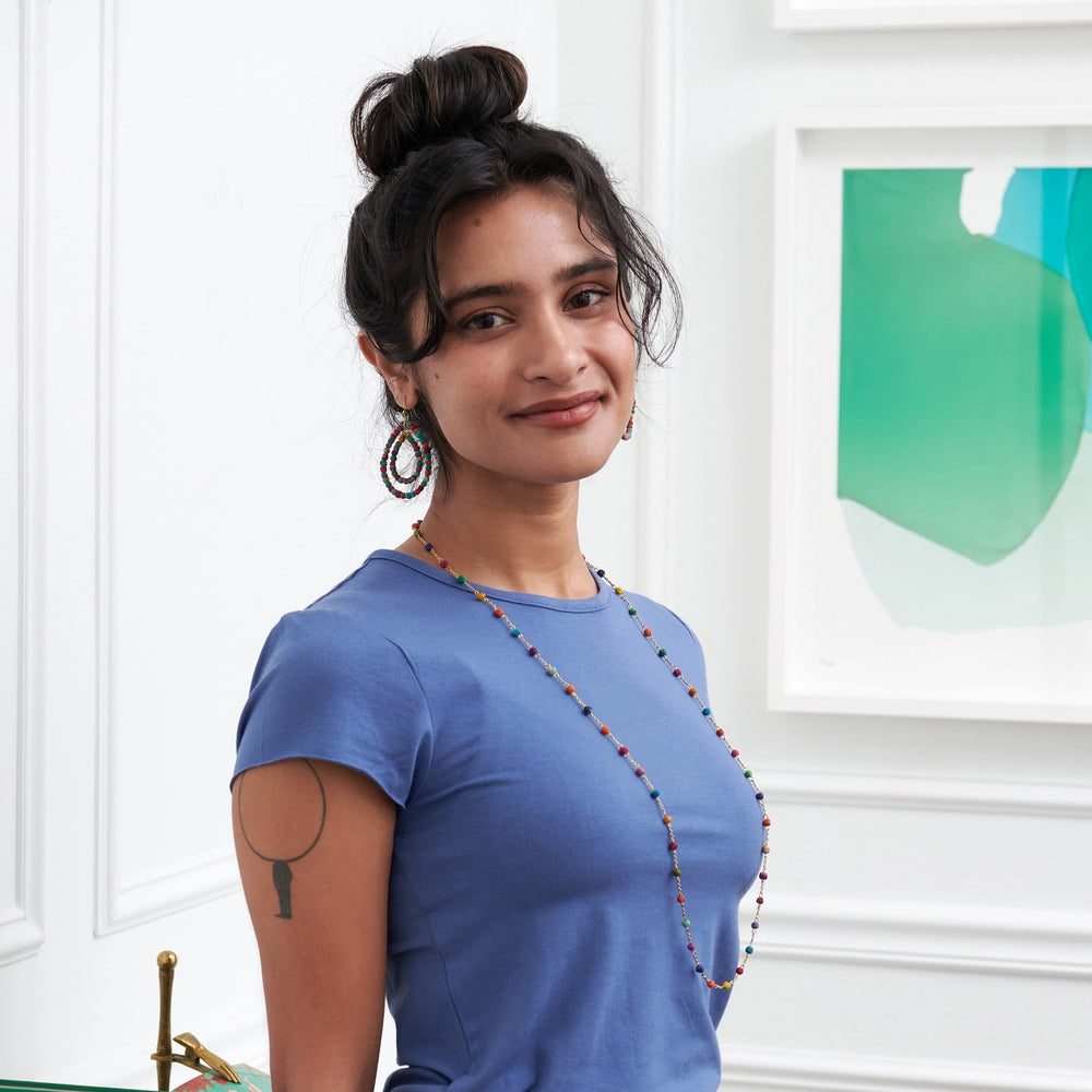 Woman wearing a colorful dotted kantha milieu necklace, standing in a room with white walls and a green abstract painting.