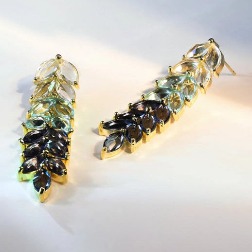 Pair of earrings with green and purple gemstones on a light background