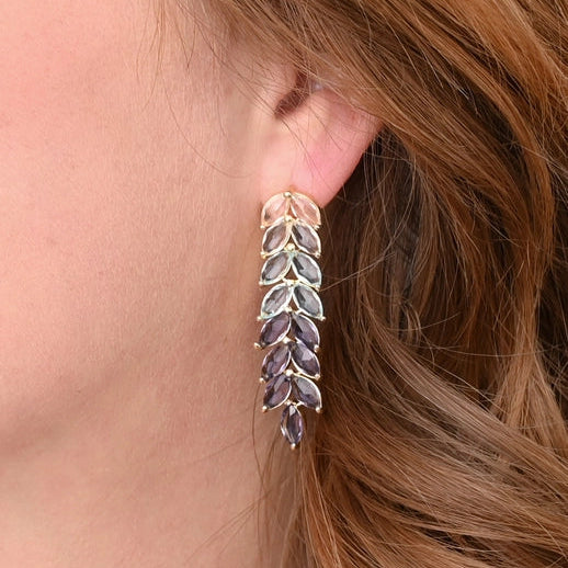 Close-up of a person wearing a leaf-shaped earring with purple stones.