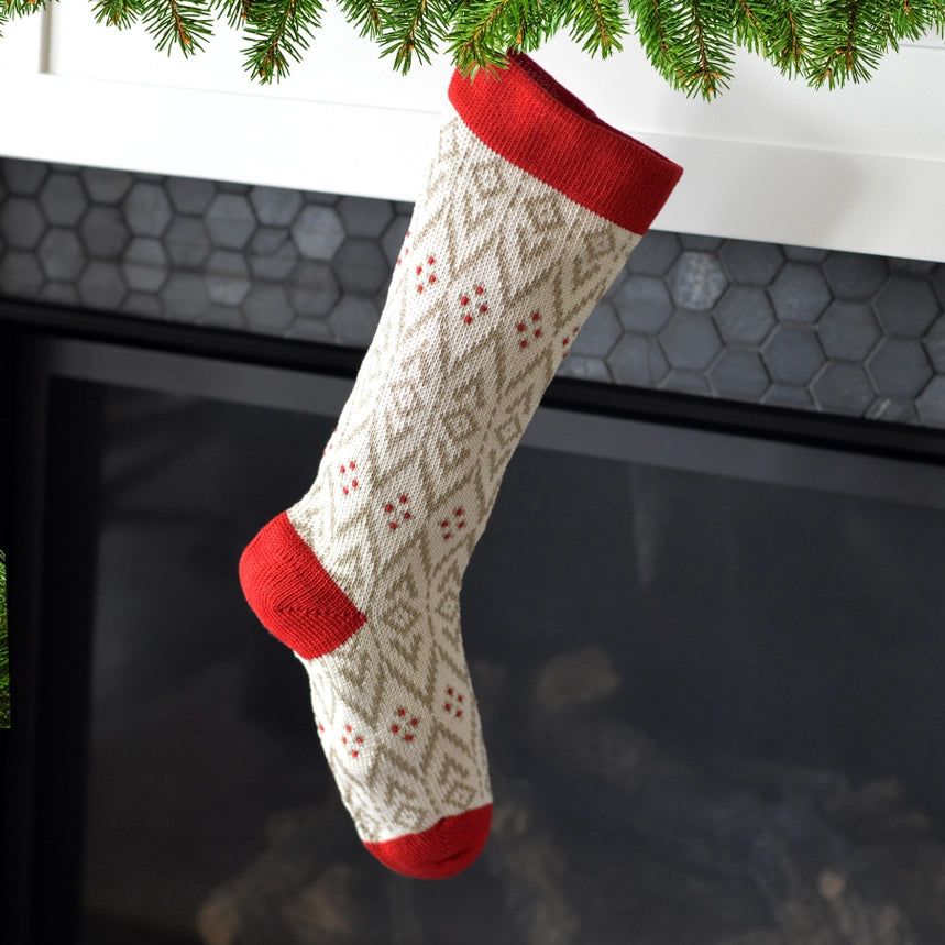 Knitted Christmas stocking with red trim hanging by a fireplace.