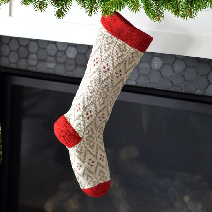 Knitted Christmas stocking with red trim hanging by a fireplace.