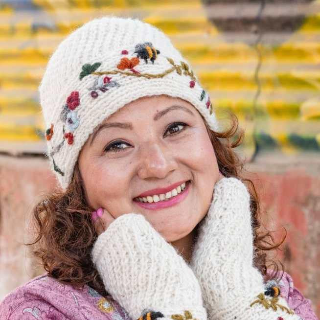 Woman wearing a white embroidered hat and mittens with a pink patterned coat against a blurred background.