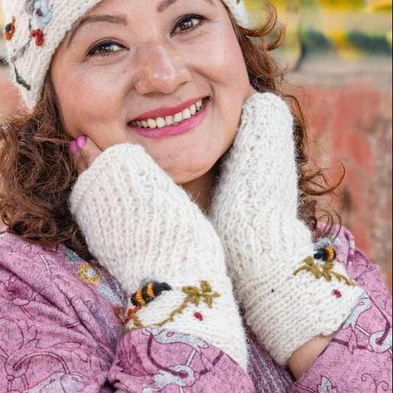Woman wearing a white embroidered hat and fingerless gloves with a pink patterned coat against a blurred background