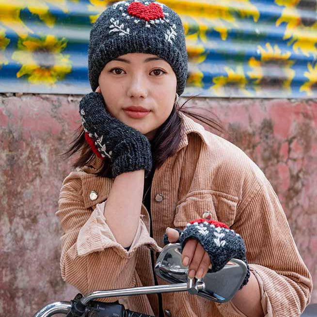 Person wearing a brown coat and black knitted hat with a red flower, sitting on a motorcycle.