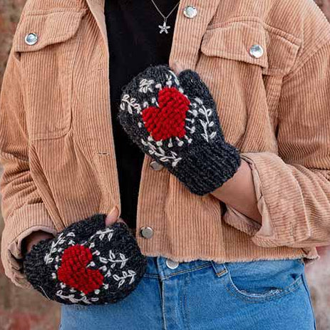 Person wearing a brown jacket, black beanie, and blue jeans with red and black patterned gloves against a colorful wall.