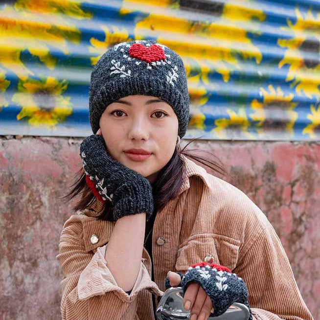 Person wearing a brown coat and black knitted hat with a red flower, sitting on a motorcycle.
