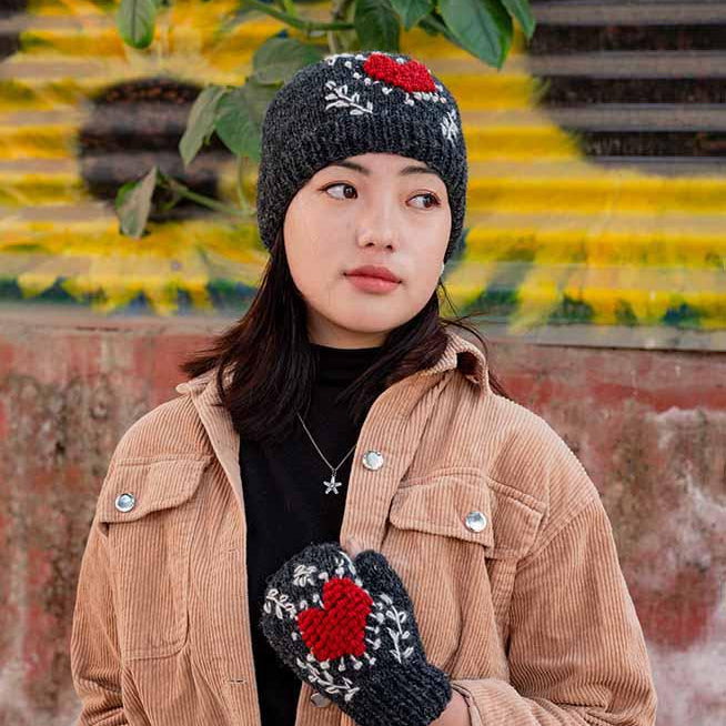 Person wearing a brown jacket, black beanie, and blue jeans with red and black patterned gloves against a colorful wall.
