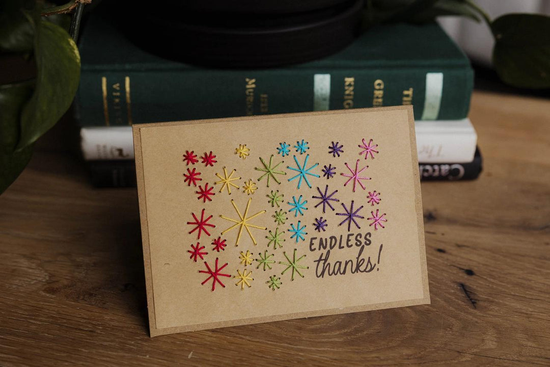 Card with colorful star patterns and 'Endless thanks!' text on a wooden surface with books in the background.