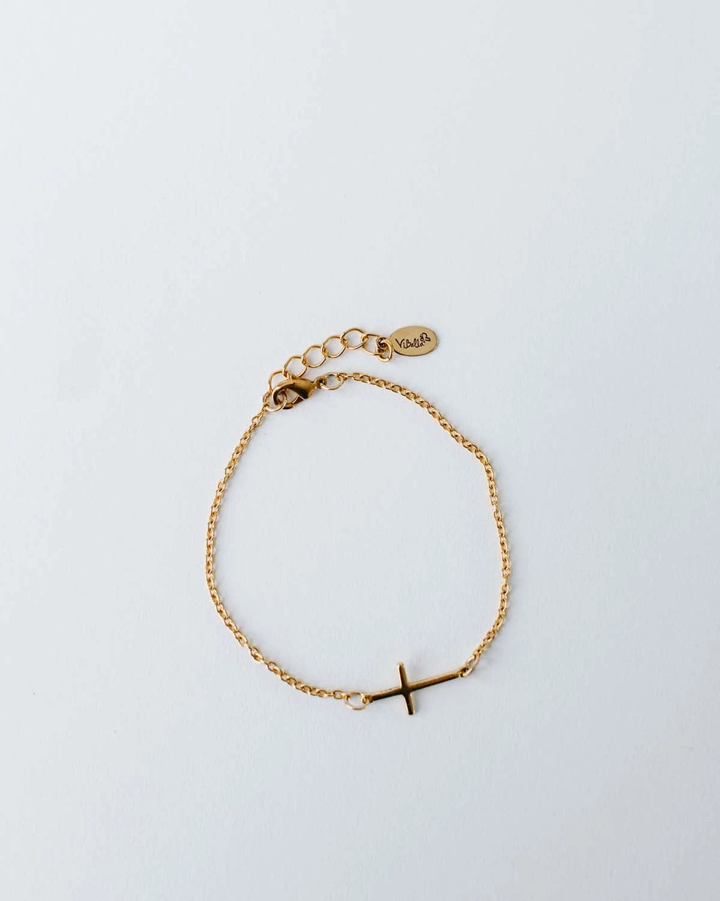 Gold bracelet with a small cross charm on a light gray background