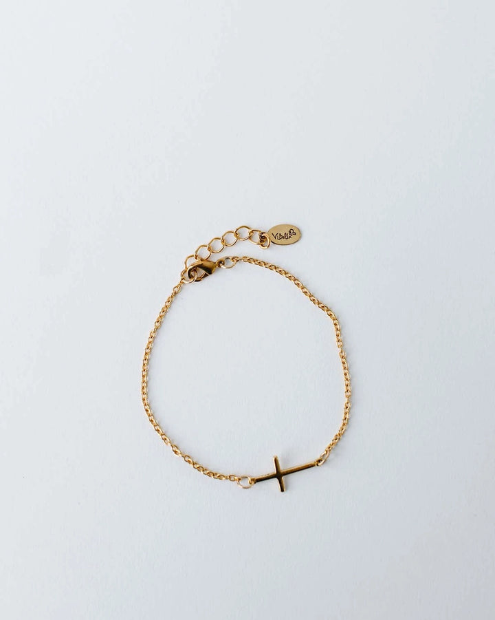 Gold bracelet with a small cross charm on a light gray background