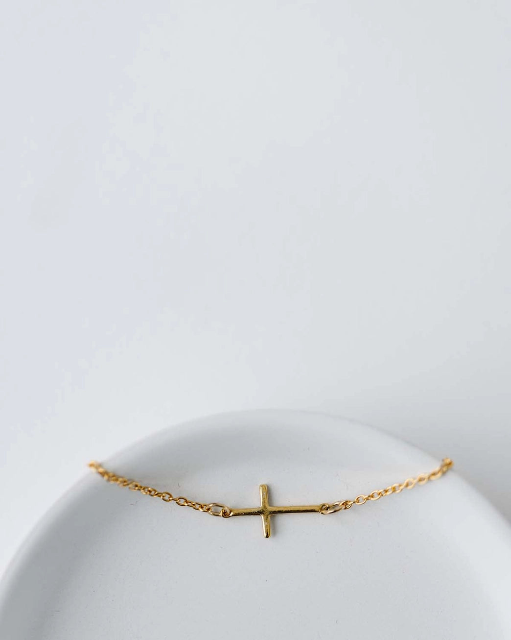 Gold cross bracelet on a white plate with a light gray background