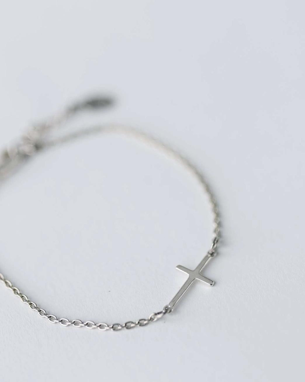 Silver bracelet with a cross charm on a light gray background