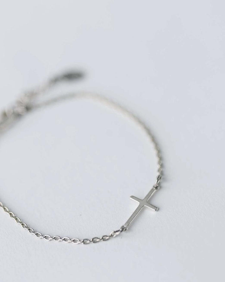 Silver bracelet with a cross charm on a light gray background
