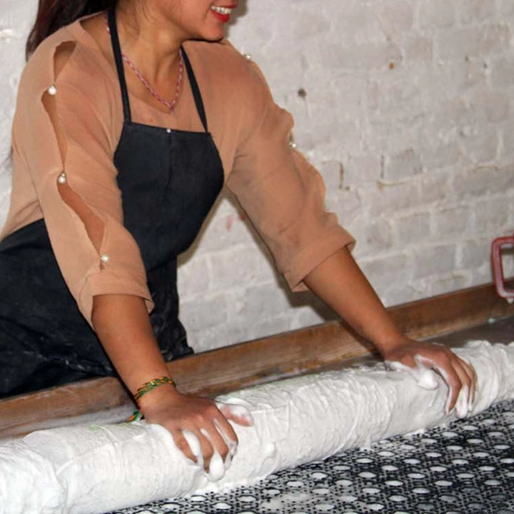 Person rolling out wool on a stone surface with a textured wall background