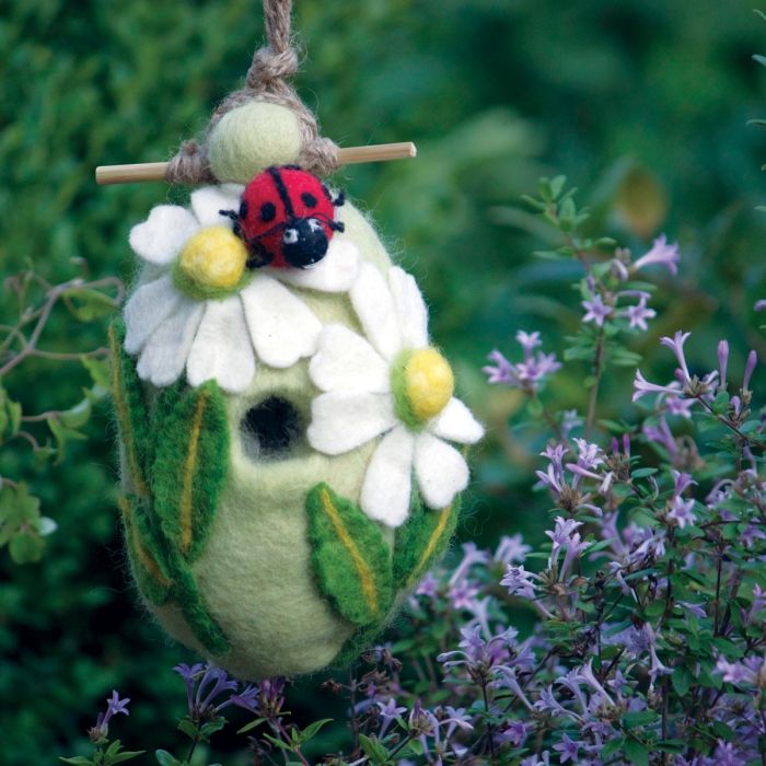 Decorative felted birdhouse with ladybug on flowers in a garden setting