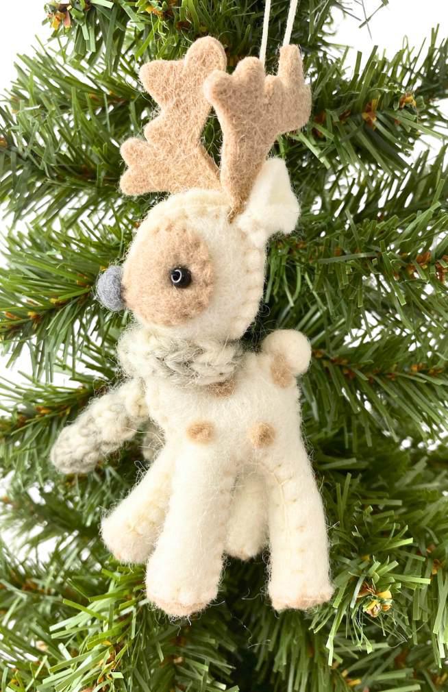 Small white reindeer ornament with antlers wearing a white scarf hanging on a Christmas tree.
