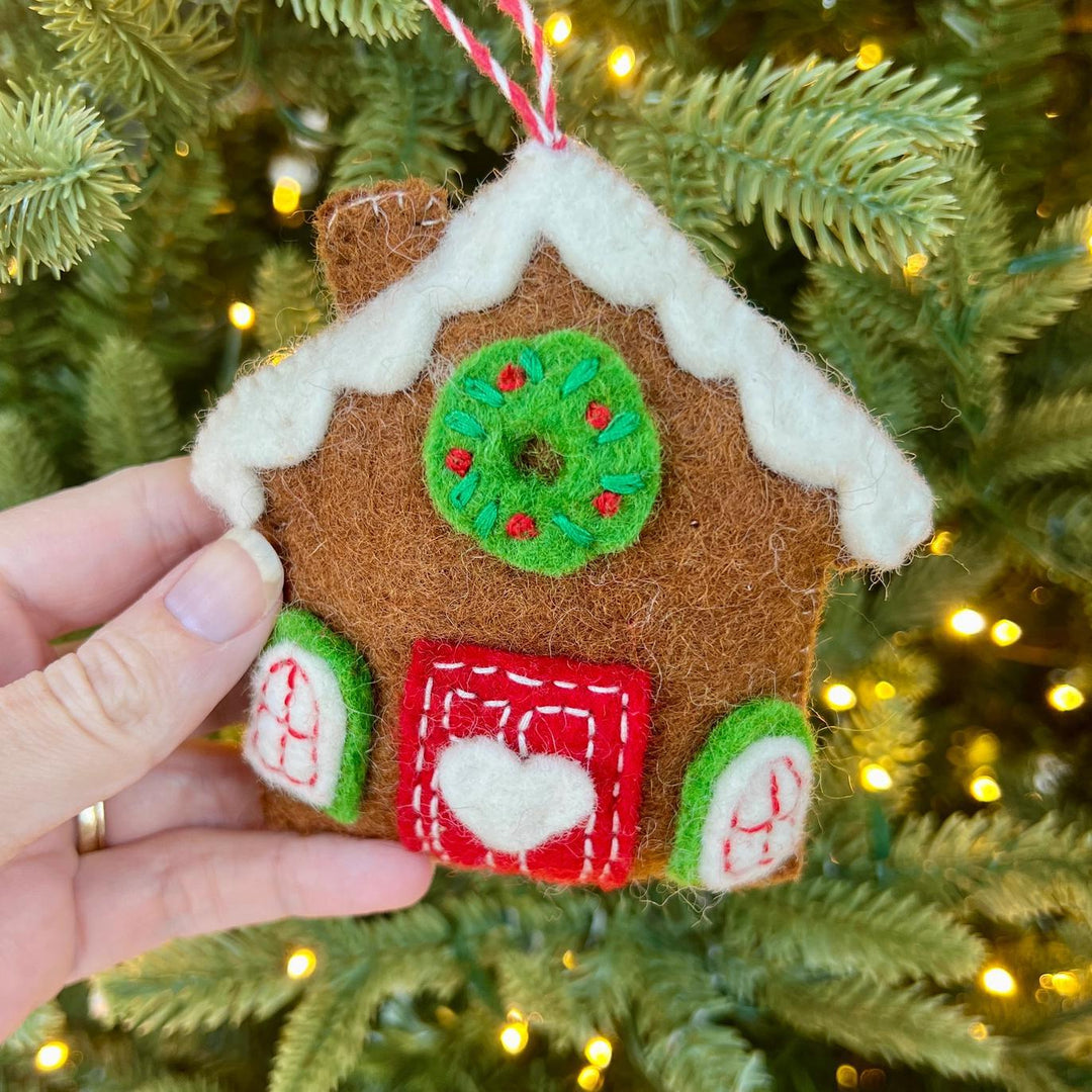 Hand holding a gingerbread house ornament against a Christmas tree background