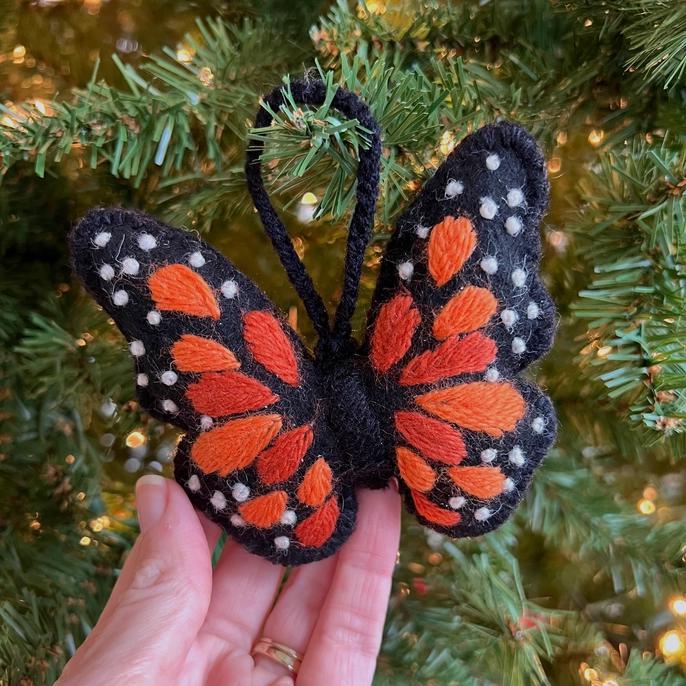 A handmade felt wool ornament in the shape of a Monarch butterfly, with black and orange colors, held in a person's hand.