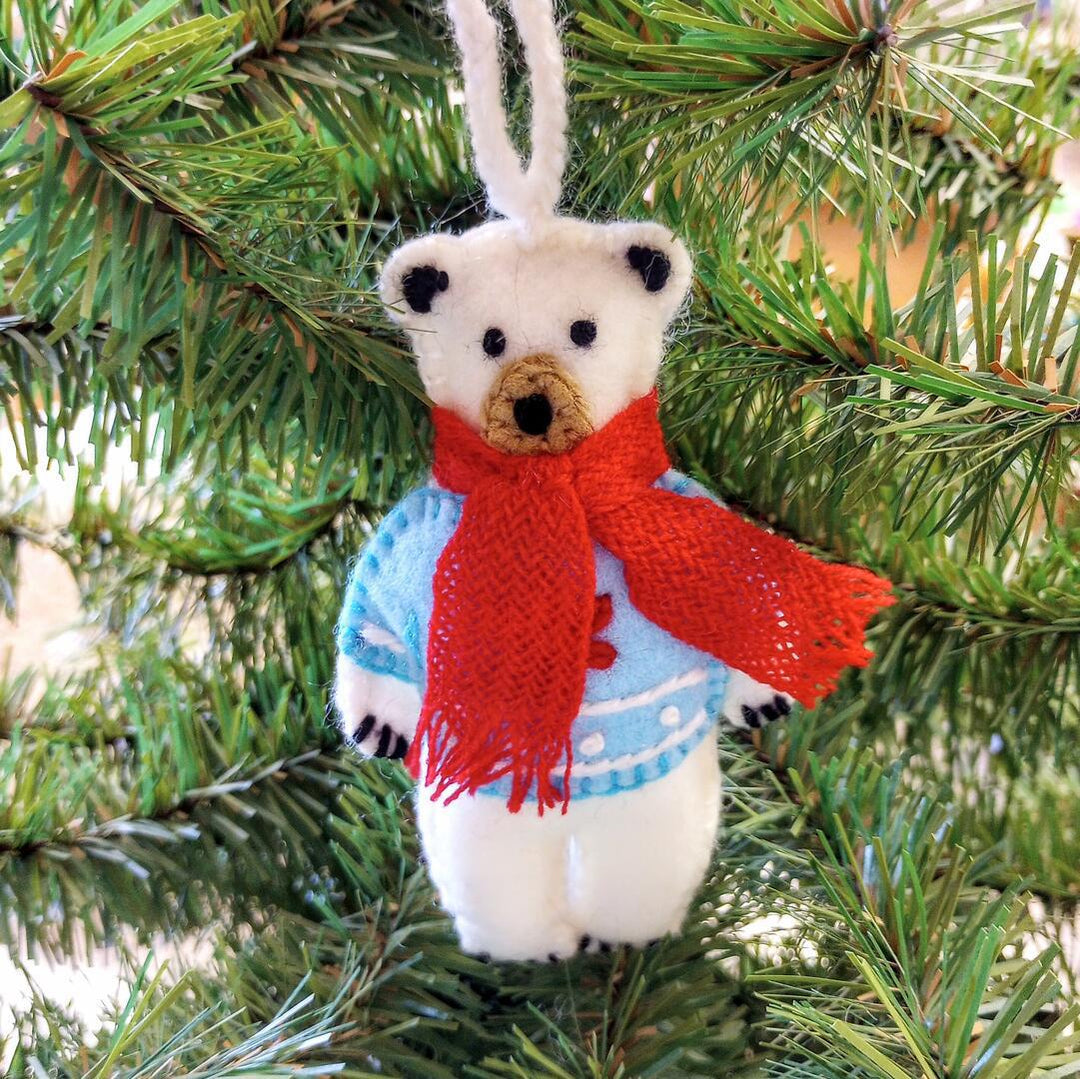 Decorative bear ornament with a red scarf hanging on a Christmas tree.